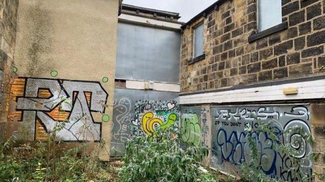 Rear view of the building showing windows boarded up and walls covered in graffiti