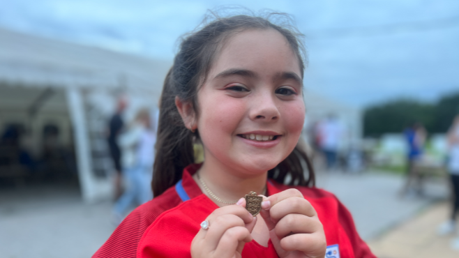 Elsie, smiling and holding a necklace up towards the camera