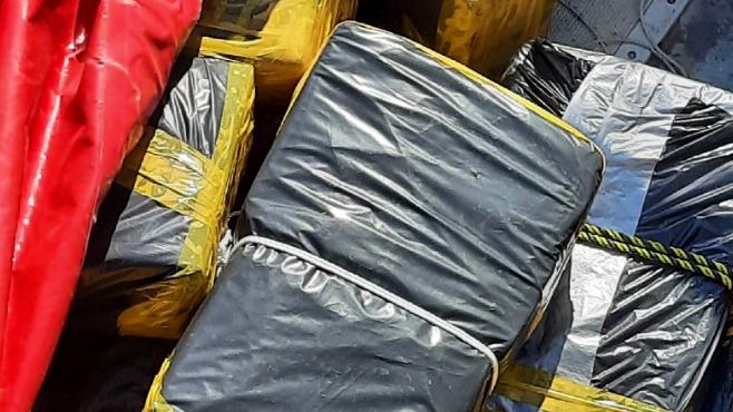 A close up of a block of drugs wrapped in black bin bag and secured with white string and yellow tape. 