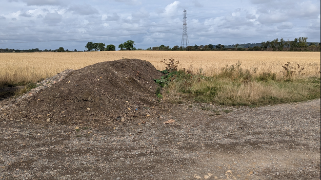 A mound of dirt in a field with a pylon in the distance