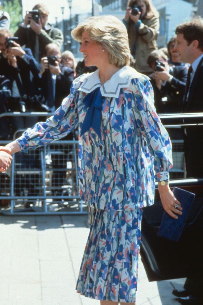 Diana, Princess of Wales, wearing a Liberty print maternity suit designed by Jan Van Velden, while pregnant with Prince Harry, visits the Albany Centre on May 23, 1984 in Deptford, United Kingdom.
It is a pastel floral outfit in blue with bits of pink, a large Peter Pan collar and a blue ribbon at the neck.