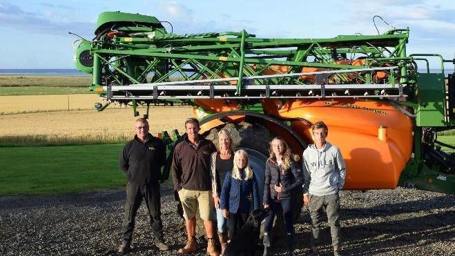 Rod Smith with his family stand in front of a combine harvester. The sea is just visible behind it.