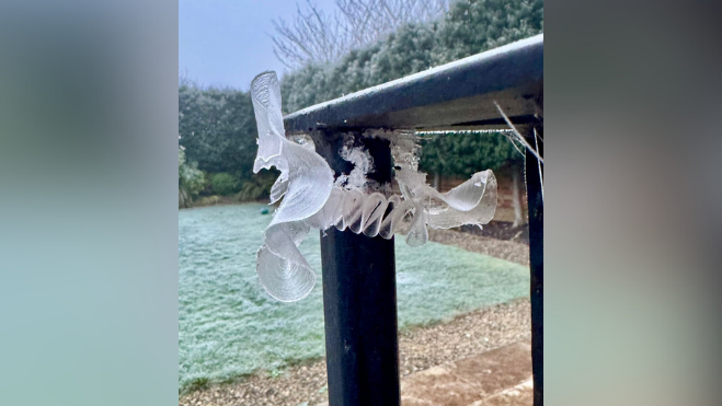 An ice flower formation on a balcony rail. It is wavy and slightly cracked.