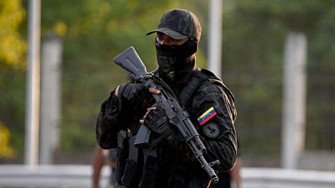 A member the National Guard stands guard in camouflage and with a gun at an entrance to Fuerte Tiuna