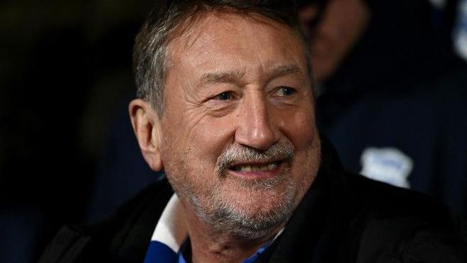 Steven Knight pictured smiling while wearing a blue and white scarf at a Birmingham City game