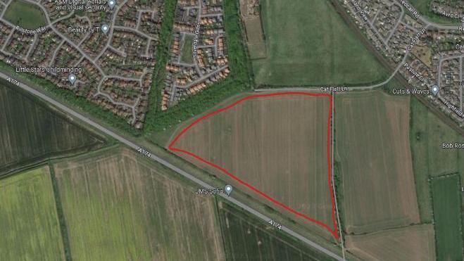 An aerial view of the application site which is highlighted with Silverdale Gardens immediately to the northwest. The development site is highlighted with a red line, which is roughly triangular in ship. It is located in a field. Other fields lie to the east and south of the site.