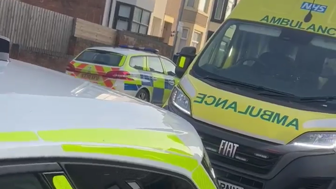 Police and ambulance vehicles are parked close by one another on a residential street.