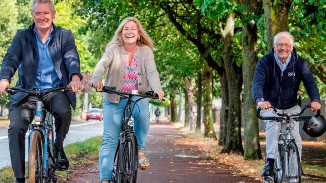 Three cyclists ride along a tree-lined cycle lane