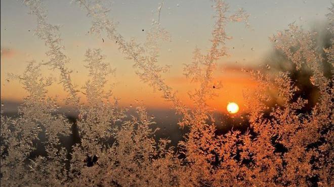 Frost on a window, with a deep orange sunrise in the background.