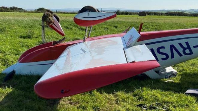 A red and white light plane upside down on the grass