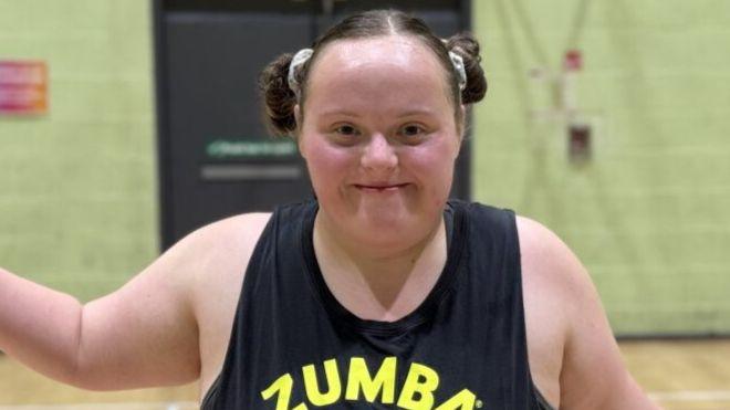 Hannah, who has brown hair tied into two bunches and is wearing a black vest, smiles at the camera