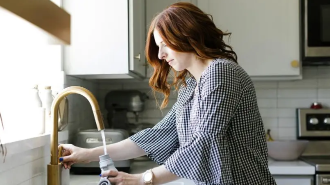 A woman stood at a sink filling a bottle of water (stock image)