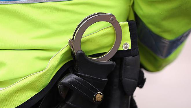 Handcuffs poking out of a police officers back pocket. The officer wearing the luminous police uniform jacket.