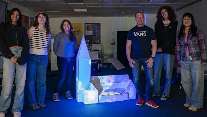 Six members of the team, standing alongside a scale model to the church with illuminated designs projected onto it