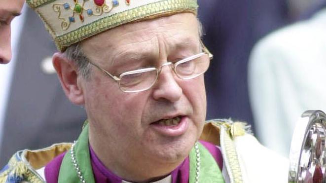 Anthony Pierce wearing a bishop's mitre with a gold trim along the bottom. He is clean-shaven and wearing glasses, and is looking down. The top of his robes and his clerical collar can just be seen in the shot. 