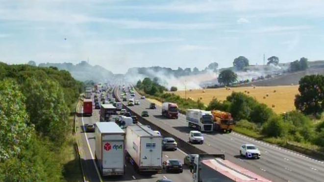Heavy traffic on a motorway with a field on fire next to it