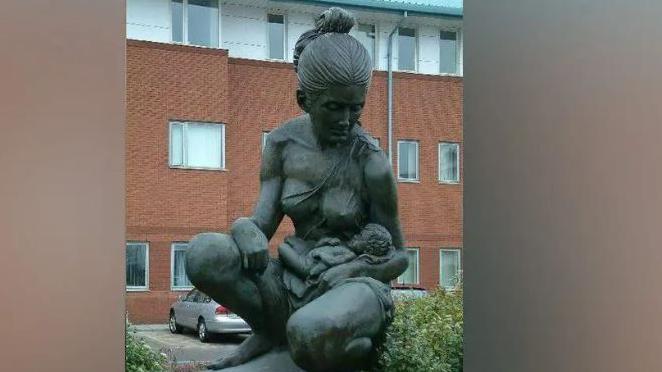 A statue of a woman holding a baby outside a brick and clad hospital building 