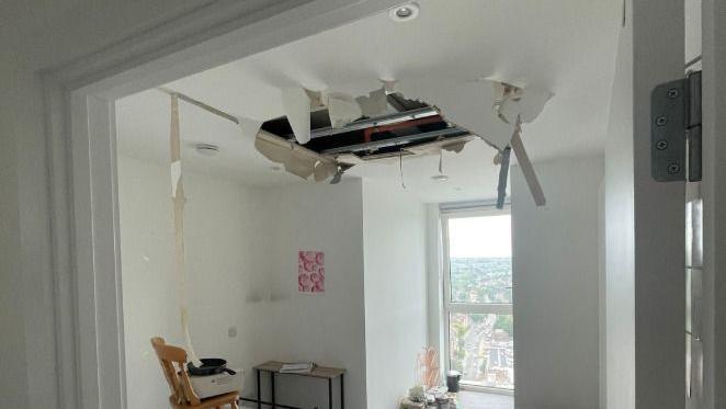 A ceiling in a flat has collapsed, with plaster and insulation hanging down into a bright living space.