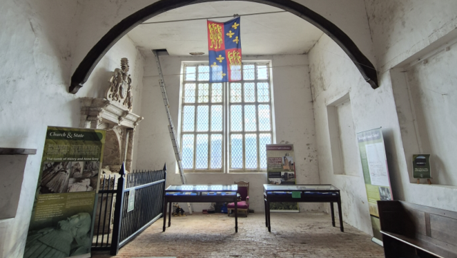 An arch in a whitewashed chapel with a large window and display cabinets 