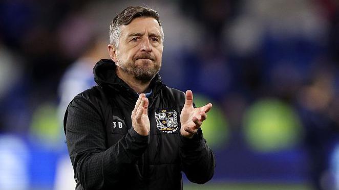 Jon Brady claps the crowd after a Port Vale match. He is wearing a black club hoodie.