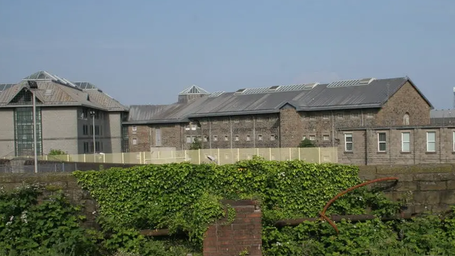A modern-day exterior photo of Cardiff prison. Within the bleak grey stone walls and sturdy gates still lie the remains of dozens of executed inmates