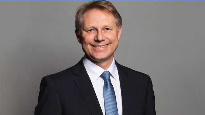 A publicity headshot image of David Morris, smiling in a suit with light blue tie