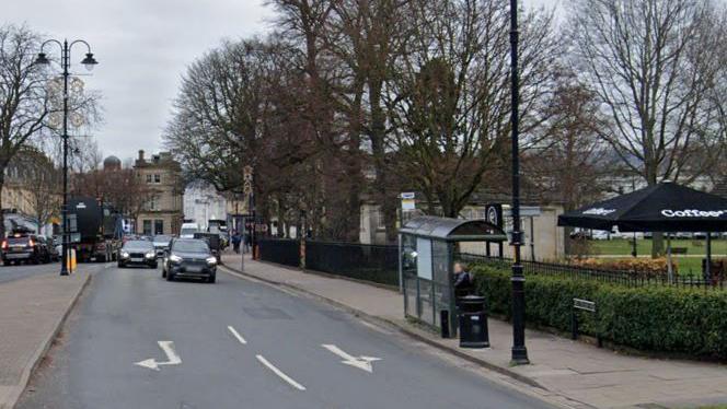 A bus stop on a road in Cheltenham next to a park