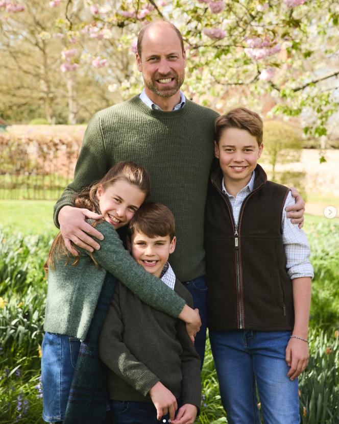 A portrait image of Prince William with George, Charlotte and Louis standing against a garden. All four look towards the camera and smile.