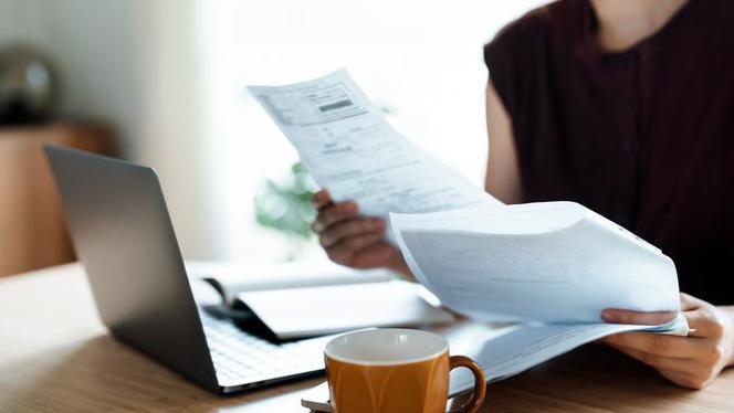 A stock image of a woman looking at her laptop and some bills