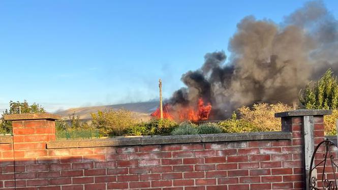 Orange flames are visible with black smoke in this shot taken over a brick wall.