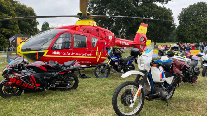 An air ambulance helicopter is stationary in a field with motorbikes parked around it