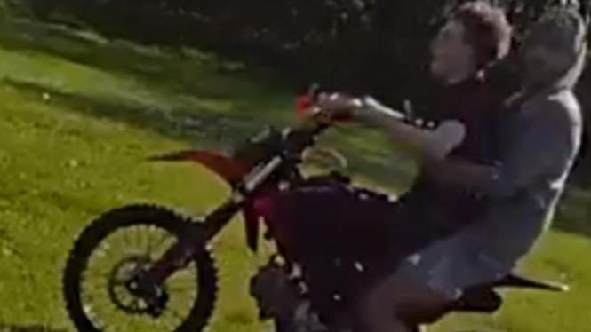A photograph taken from police bodyworn video showing two young men on a scrambler bike in Stowlawn Green. The one on the front of the bike is holding the handlebars and looking straight forwards. He is wearing a black T-shirt and black trousers and trainers. The other sitting behind him is wearing shorts and trainers and a grey hoodie and he has turned his head to look at the person taking the image.