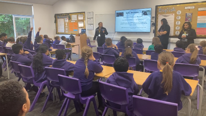 Pupils in a purple uniform are sat with their back to the camera listening to staff and Ronan's family talk in their classroom.