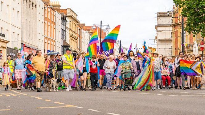 The start of the Pride march in Leamington with many people holding rainbow banners between the Georgian buildings of the town