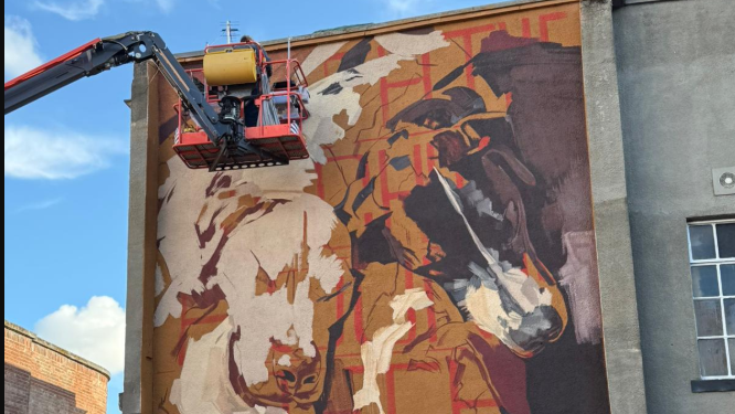 An artist on a crane finishing off a mural of sleeping dogs