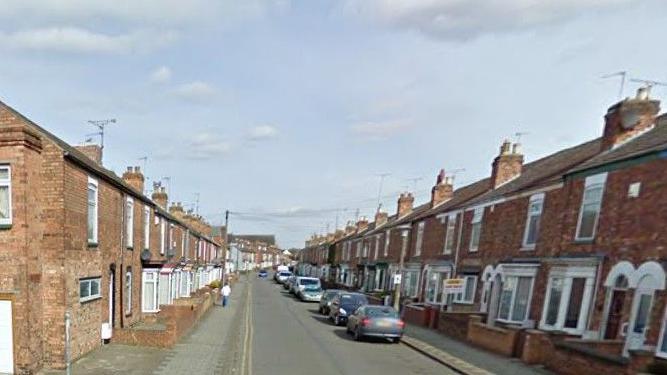 View looking down the road of the chimney-topped terraced houses on Drake Street, with cars parked outside 