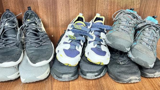 Six pairs of trainers are piled up in a box. There are black and grey pairs  and one with blue laces.