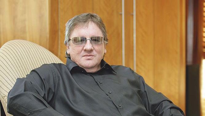 Well-known South African businessman Douw Steyn is seen wearing a black shirt and glasses as he sits in a chair.