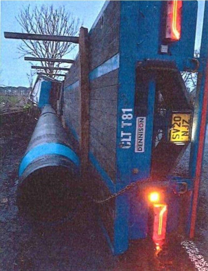 A large lorry tipped on its side on a road with a tree in the background