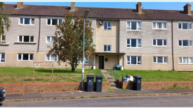 A three storey block of flats with a grass verge outside and bins on the pavement