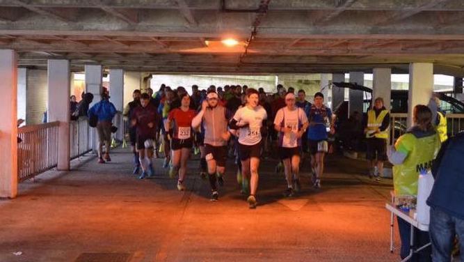 About 60 runners setting off at the start of a marathon inside a multi-storey car park