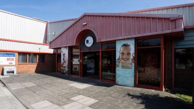 The outside of the leisure centre has a posted of a smiling woman in a swimming pool. 