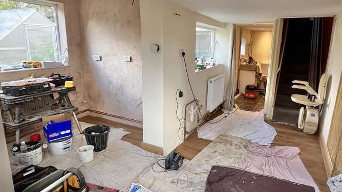 Dust sheets are on the floor of the Shortt's kitchen area, which has been stripped of all units back to plaster. A work bench is to the left hand side, surrounded by buckets and various building materials.