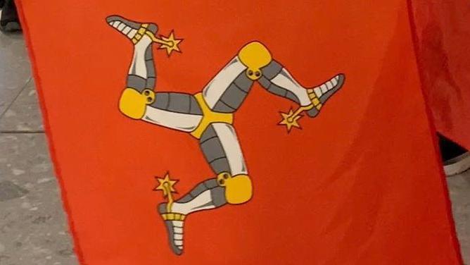 A close-up of three Manx flags, which are red with a yellow, white and grey three-legs of man symbol.