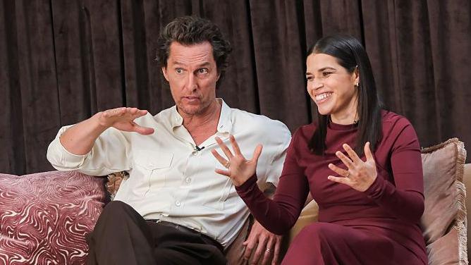 Matthew McConaughey and America Ferrera in conversation on a sofa in smart casual clothes