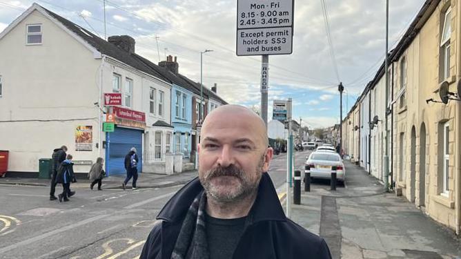 Councillor Alex Paterson from Medway Council standing on Richmond Road, Gillingham next to a School Streets Scheme restrictions sign as children walk to school on the opposite footpath
