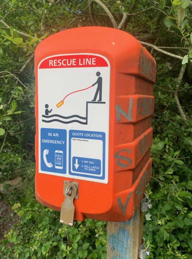A vandalised rescue line. It is bright orange and there is graffiti on the side of it.