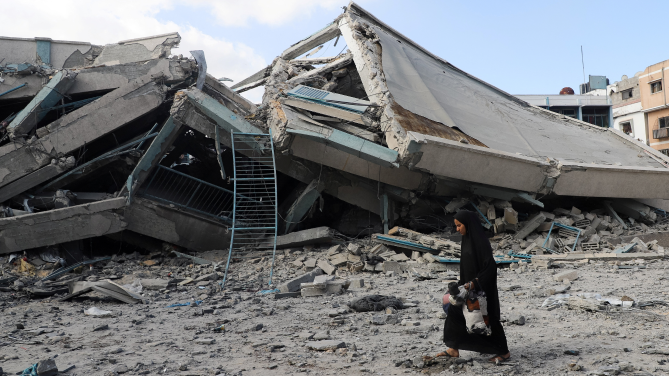 A Palestinian woman carries belongings as she walks amid debris at a United Nations school where displaced people were taking shelter, after it was hit in overnight Israeli strikes, amid an Israeli military operation, at Zeitoun neighbourhood in Gaza City, October 1