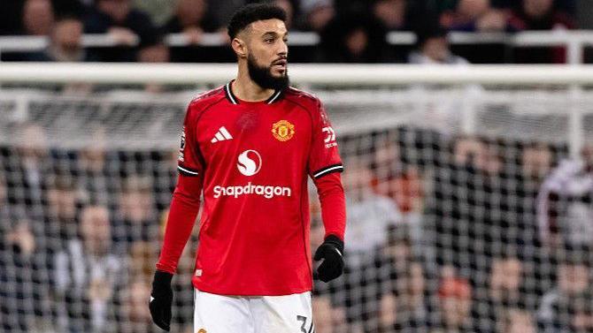 Manchester United defender Noussair Mazraoui on the pitch during the game against Newcastle. A home section of the crowd is out of focus in the background.