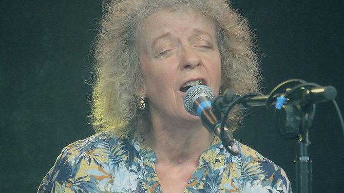 Alison wearing a blue and yellow blouse singing into a microphone